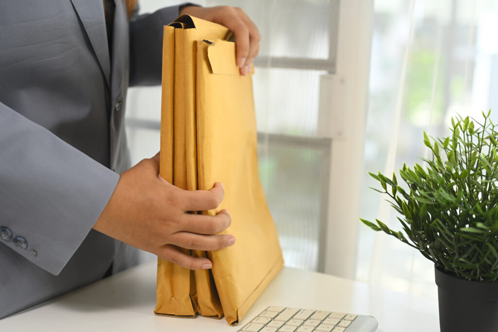 cropped shot of businessperson organizing important documents in envelopes at office desk